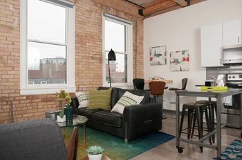 A living room with a black couch and a green rug.